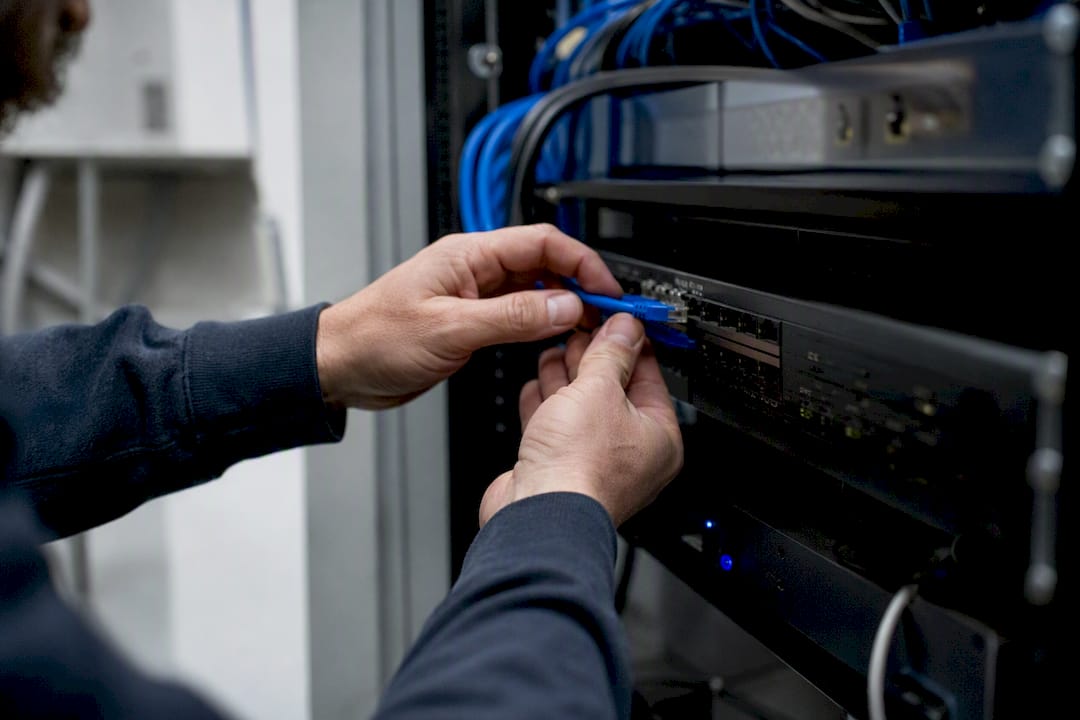 Hands reconnecting network cable inside IT rack
